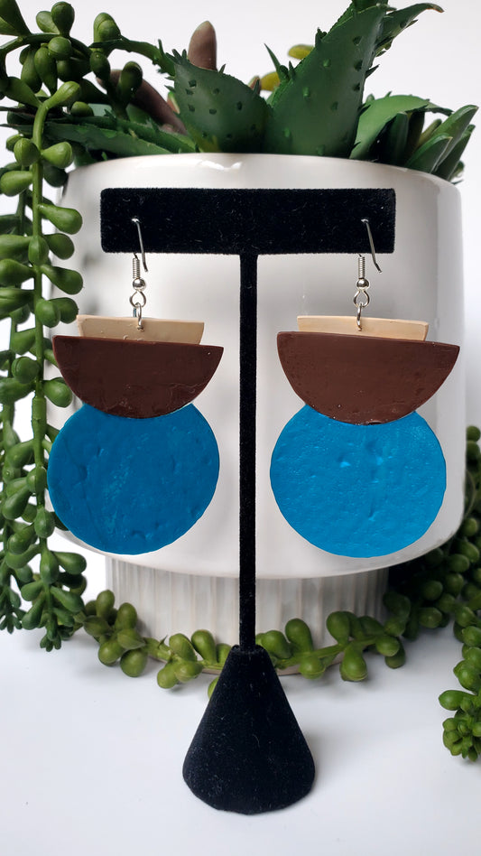 Pair of earrings on a stand with green plants in the background