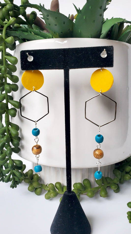 Yellow and black geometric earrings on a stand with green foliage in the background